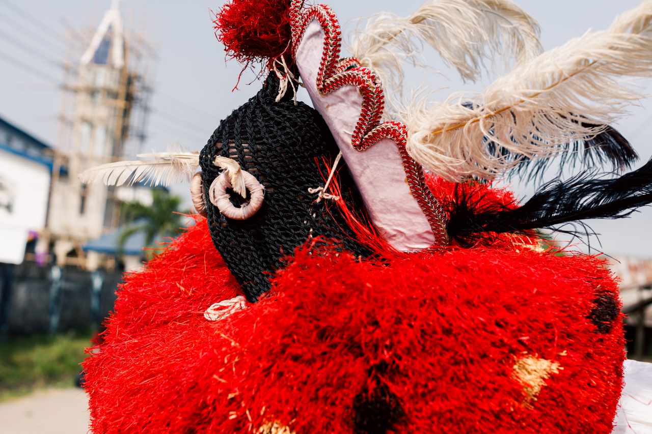 A close-up of a colorful traditional masquerade costume with feathers and decorations in an outdoor setting.