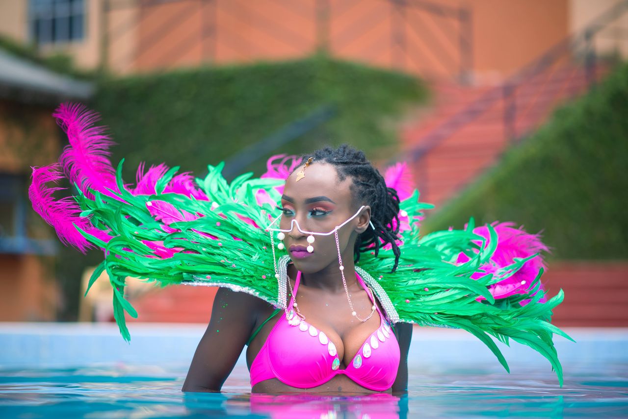 African woman in a colorful, feathered costume posing in a swimming pool.